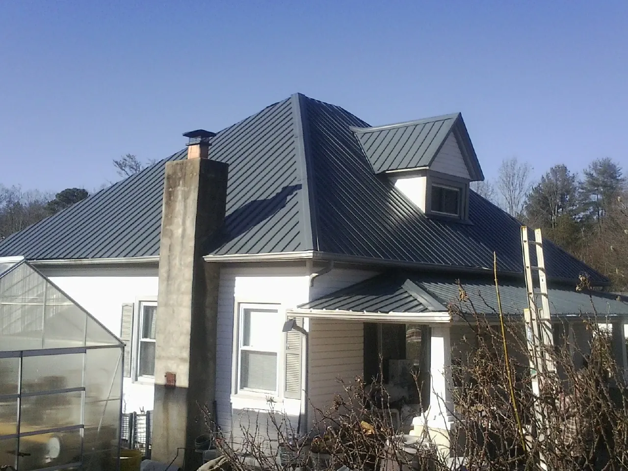 Dark blue standing seam metal roof on a white farmhouse with dormer — Slate & Tile Roof Repair by Roofing Brothers in Tryon
