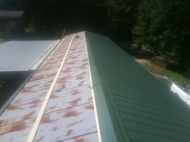 Old rusted panels beside newly installed green metal roofing — Wind Damage Roof Repair by Roofing Brothers in Tryon