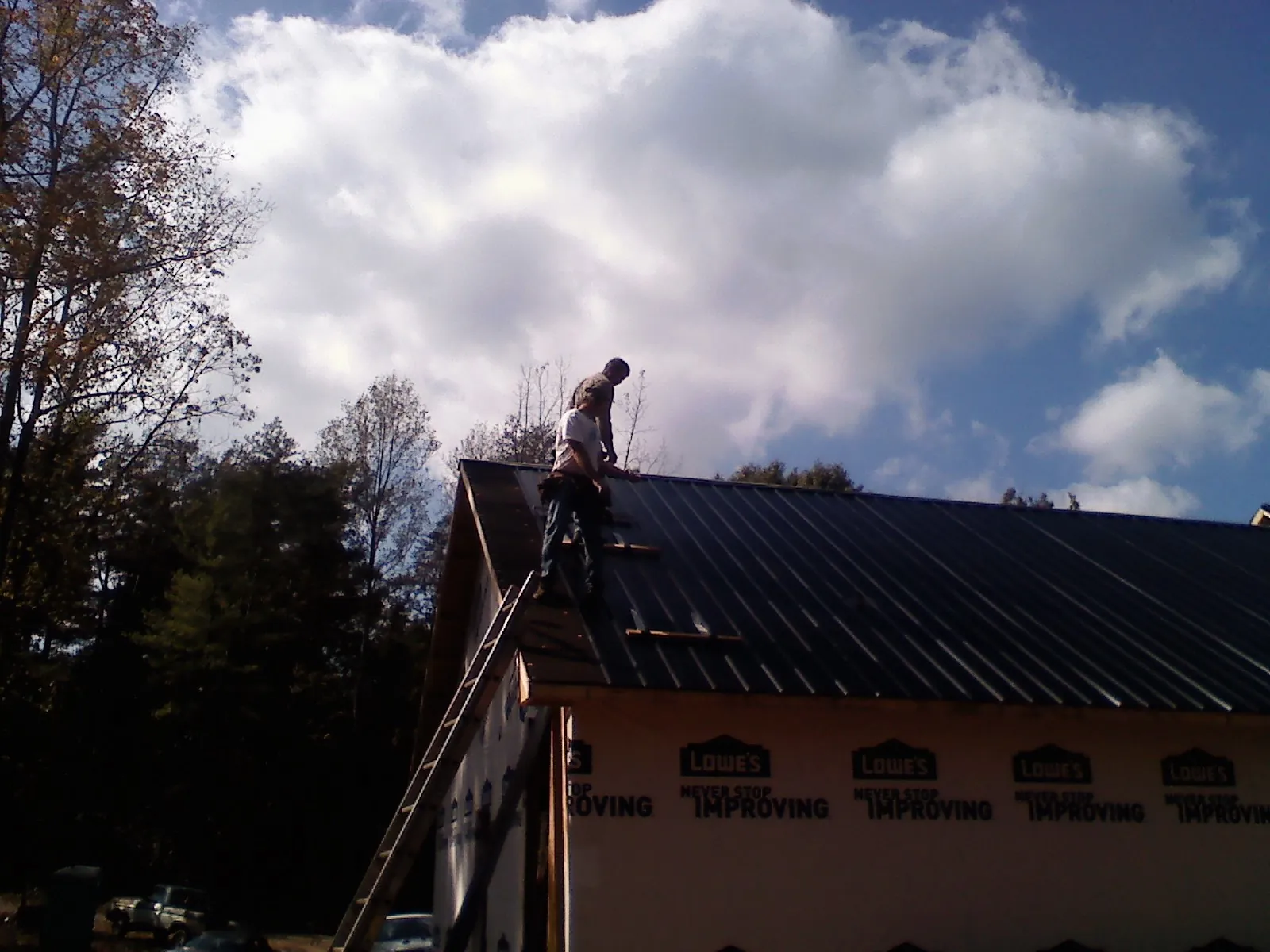 Roofer fastening dark metal panels high against a cloudy sky, from a Roof Inspection job in Tryon