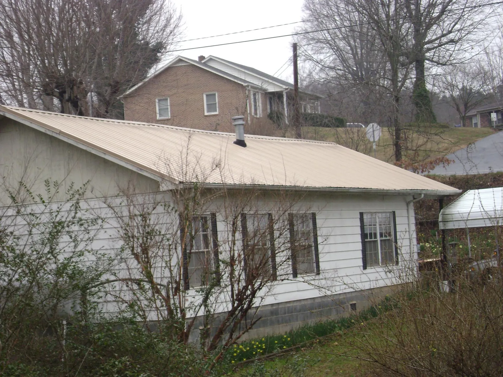 Tan metal roof on a white sided house set into a hillside — Commercial Roofing by Roofing Brothers in Tryon